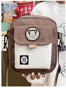 Detail of adjustable strap and bear patch on brown and white canvas crossbody bag