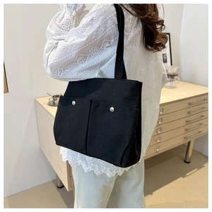 Detail of a black canvas tote bag with dual front pockets and silver metal buttons for daily use