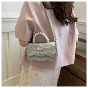 Detail einer silbernen Falten-Handtasche mit Perlengriff und Metall-Schleife