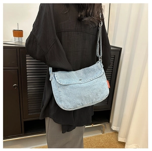 Detail view of a light blue denim crossbody bag with flap and red brand side label