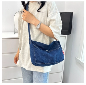 Detail view of a dark blue denim crossbody bag with a magnetic flap and red woven label