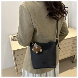 Détail du sac seau noir en cuir avec un charm de monstre en peluche et une bandoulière fine