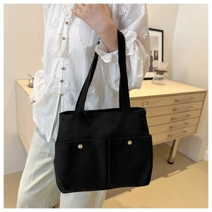 Detail of black canvas tote bag showing front pockets and gold metal snap buttons