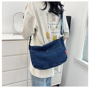 Detail of the large capacity dark blue denim messenger bag with vintage metal buckle and red label