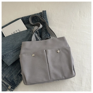 Detail of grey canvas tote bag featuring dual front pockets and silver metal buckles