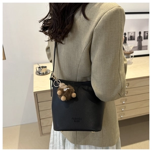 Détail du sac seau en cuir noir avec breloque en peluche sur un blazer beige chic