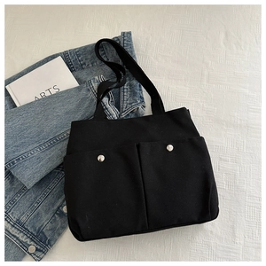 Detail of black canvas tote bag with front pockets and silver metal snap buttons