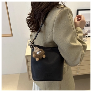Détail d'un sac seau noir en cuir grainé avec charmant pendentif monstre en peluche brun