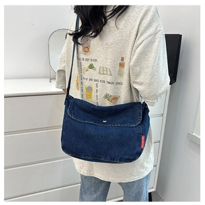 Detailed view of dark blue denim crossbody bag featuring silver snap closure and side label