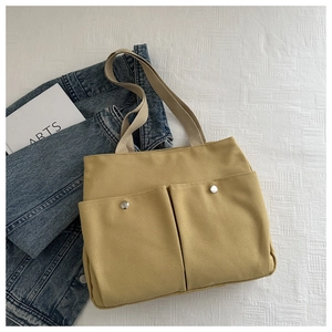 Detail of yellow canvas tote bag featuring dual front pockets with silver metal snap buttons