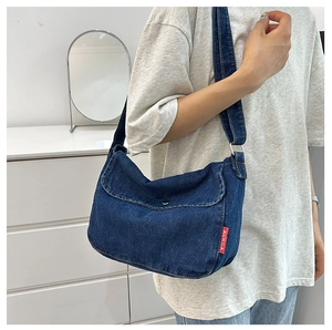 Detail showing the dark blue denim messenger bag with red brand label and wide strap