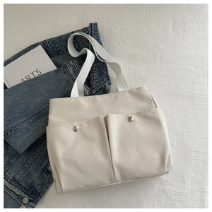 Detail of off-white canvas tote bag featuring double front pockets and metal snaps