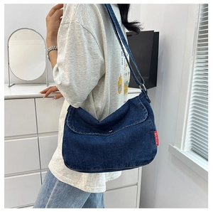 Detail view of large blue denim crossbody bag with red logo tag shown on a model