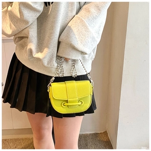 Detail of a bright yellow saddle bag with lychee texture leather and silver chain strap