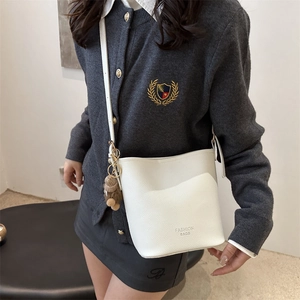 Sac seau minimaliste en cuir blanc avec pendentif ours porté par un mannequin pour femme
