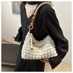 Close-up of white bubble texture handbag with wooden bead strap on model in black dress
