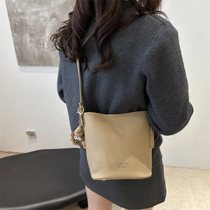 Sac seau chic en cuir beige avec imprimé mode et breloque peluche sur un mannequin