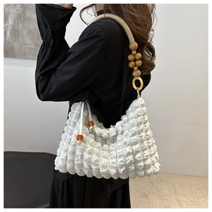 Detail of white pleated handbag with unique wooden bead strap and colorful charm