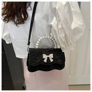 Detail of black velvet crossbody bag featuring silver bow clasp and pearl handle