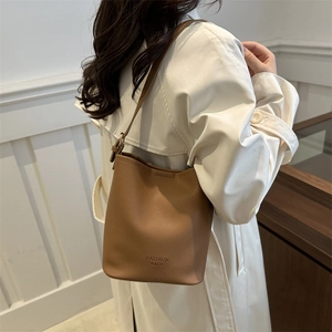 Sac seau minimaliste en cuir marron avec bandoulière réglable et détail de texte embossé