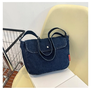 Detail of blue denim shoulder bag with silver buckle and red label on a chair