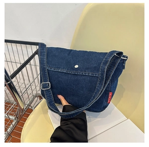 Detail of a dark blue denim messenger bag with adjustable strap and red brand tag