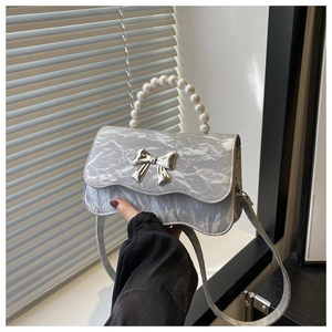 Detailed shot of silver bow handbag featuring pearl handle and pleated metallic texture