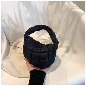 Close-up of black quilted puffer handbag held against a beige blazer with soft shadows