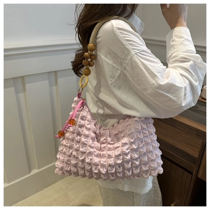 Detail of pink pleated shoulder bag featuring a woven strap with wooden beads