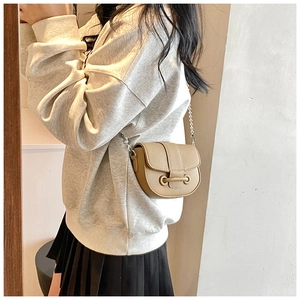 Detail view of khaki litchi grain leather saddle bag with silver chain strap on model