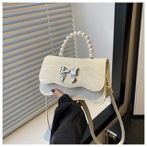 Detail of creamy white crossbody bag with pearl handle and silver metal bow ornament