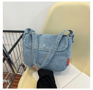 Detail of light blue denim crossbody bag with silver magnetic snap and red ACKCA brand label