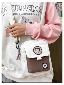 Detail of canvas crossbody bag showing a bear logo, flap pocket, and adjustable strap