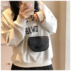 Close-up of black lychee grain leather saddle bag with silver ball chain and metal strap