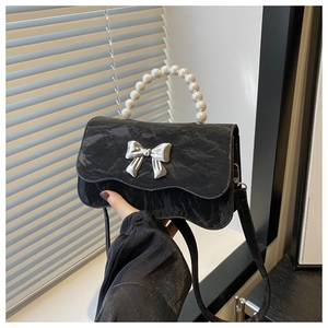 Detail of black bow handbag featuring glossy crinkled texture and pearl bead handle