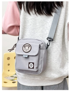 Detail view of the light grey nylon crossbody bag with cute bear patch and adjustable strap