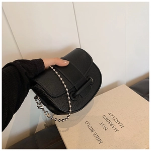Detail of black pebbled leather saddle bag featuring a decorative strap and silver bead chain