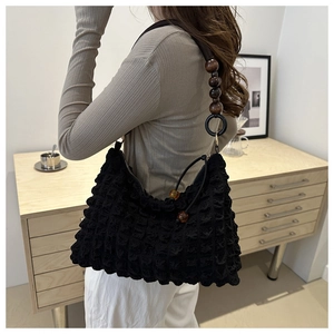 Black popcorn texture shoulder bag with brown wooden bead strap shown on model's side