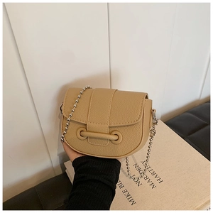 Detail of khaki saddle bag with litchi texture, metal bar buckle and silver ball chain