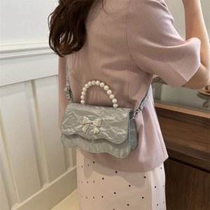 Light blue textured crossbody bag with pearl handle and silver bow decoration worn by model