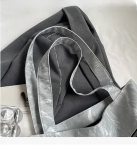 Detail of silver tote bag with metallic crinkled texture and wide double-stitched handle