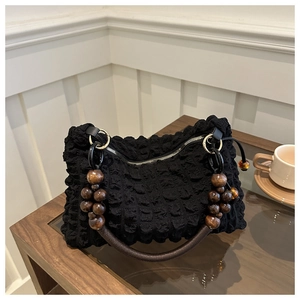 Detail of black popcorn texture handbag with vintage wooden bead handle on table