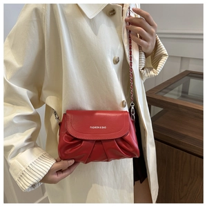 Détail du sac bandoulière rouge plissé avec chaîne porté sur un manteau beige