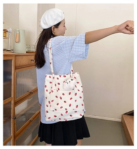 Detail of white corduroy tote bag with red strawberry print and cute plush dog charm