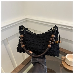 Detail of black textured bubble fabric handbag featuring vintage wooden bead handles