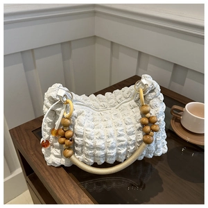 Close-up of pleated white handbag featuring wooden bead handle on a rustic wooden table