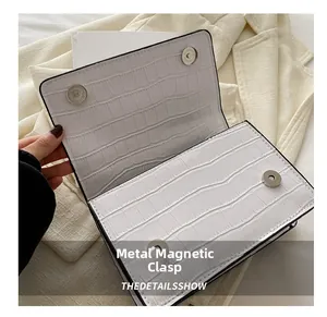 Close-up of white crocodile pattern bag featuring two silver magnetic metal snaps