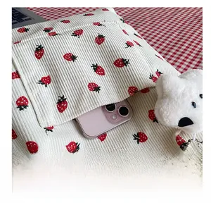 Detail view of corduroy tote bag side pocket with red strawberry pattern holding a pink phone