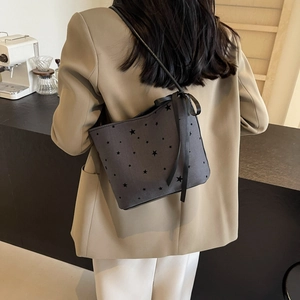 Minimalist canvas tote bag with star prints and ribbon detail worn by a model in a cafe