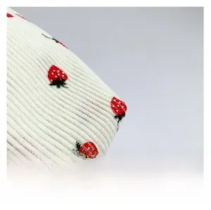 Close-up of white corduroy fabric with textured stripes and red strawberry embroidery